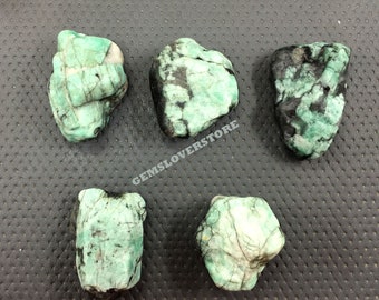 May include: Five rough, green emerald stones with black inclusions. The stones are various shapes and sizes.