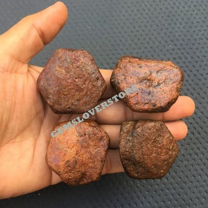 May include: Four rough, reddish-brown, star-shaped gemstones. The stones are approximately the size of a 20 pence coin.