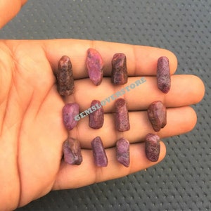 Może przedstawiać: Kolekcja 14 surowych, nieoszlifowanych, czerwonych rubinów. Rubiny są różnych rozmiarów i kształtów, o głębokim czerwonym kolorze.