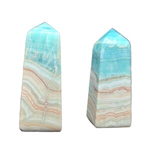 May include: Two blue-green gemstone obelisks with layered patterns of white, tan, and brown. The obelisks have a rectangular base and a pointed top. The background is plain white.