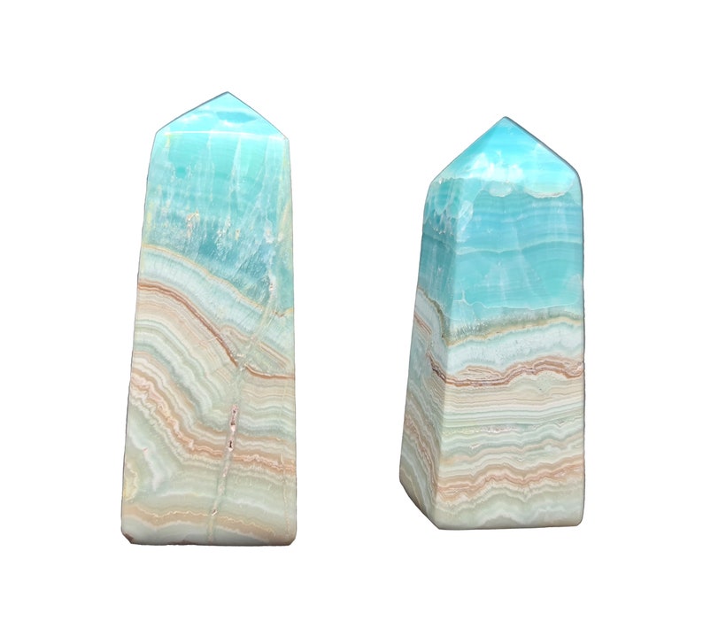 May include: Two blue-green gemstone obelisks with layered patterns of white, tan, and brown. The obelisks have a rectangular base and a pointed top. The background is plain white.