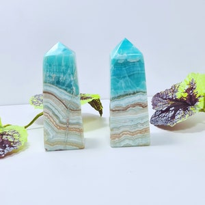 May include: Two blue and white striped crystal obelisks with a polished finish. The obelisks have a rectangular base and a pointed top. The crystals are decorated with brown and beige bands. The obelisks are approximately 5 inches tall.