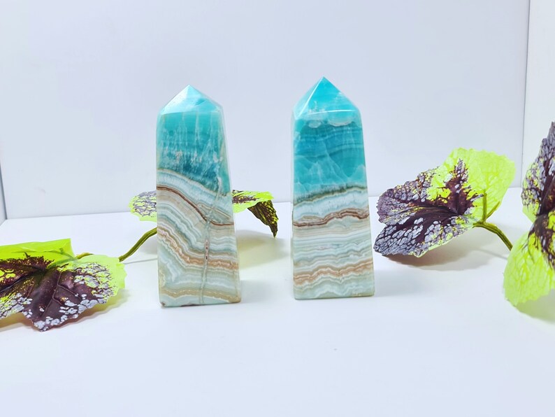 May include: Two blue and white striped crystal obelisks with a polished finish. The obelisks have a rectangular base and a pointed top. The crystals are decorated with brown and beige bands. The obelisks are approximately 5 inches tall.