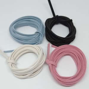 Könnte beinhalten: Vier Spulen Wildlederband in verschiedenen Farben: Hellblau, Schwarz, Creme und Rosa. Jedes Band ist aufgerollt und gebunden, wodurch die Textur und die Farbvariationen hervorgehoben werden. Ideal für Bastelarbeiten und Schmuckherstellung.