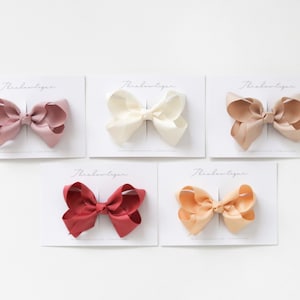 May include: Five hair bows displayed on white cards with the text "Threadboutique" printed on each card. The bows are in a range of colours, including pink, ivory, beige, peach, and red.