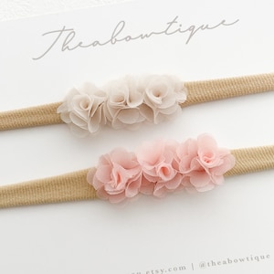 May include: Two nude elastic headbands with a cluster of three pale pink and ivory chiffon flowers on each headband.