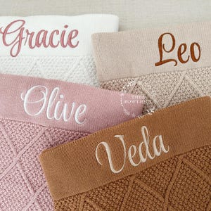 May include: Four knitted blankets in white, beige, dusty pink, and brown, each featuring a diamond-patterned texture and a smooth top band embroidered with the names Gracie, Leo, Olive, and Veda in cursive script lettering.