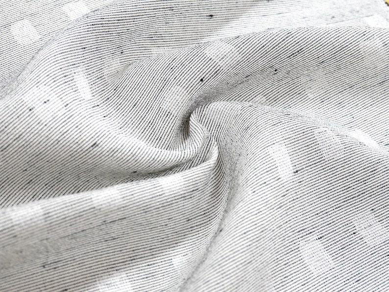 May include: Close-up of a white fabric with a subtle black and white striped pattern. The fabric is woven and has a slightly textured surface.