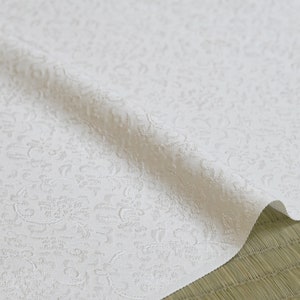 May include: White fabric with a raised, embossed pattern of small, intricate floral designs. The fabric is folded in half and has a soft, textured appearance.