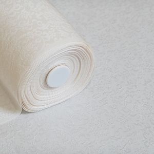 May include: A roll of white fabric with a delicate embossed pattern. The fabric is rolled up tightly and secured with a white plastic cap.