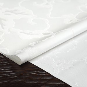 May include: White fabric with a subtle embossed pattern of clouds. The fabric is folded in half and the edges are visible.