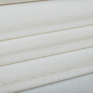 May include: White fabric with a subtle embossed pattern. The fabric is folded in layers, showcasing the texture.