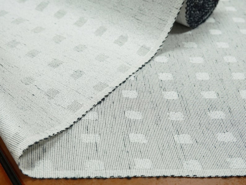 May include: White woven fabric with a subtle pattern of small, raised dots. The fabric is folded in half, showing the texture and weave.