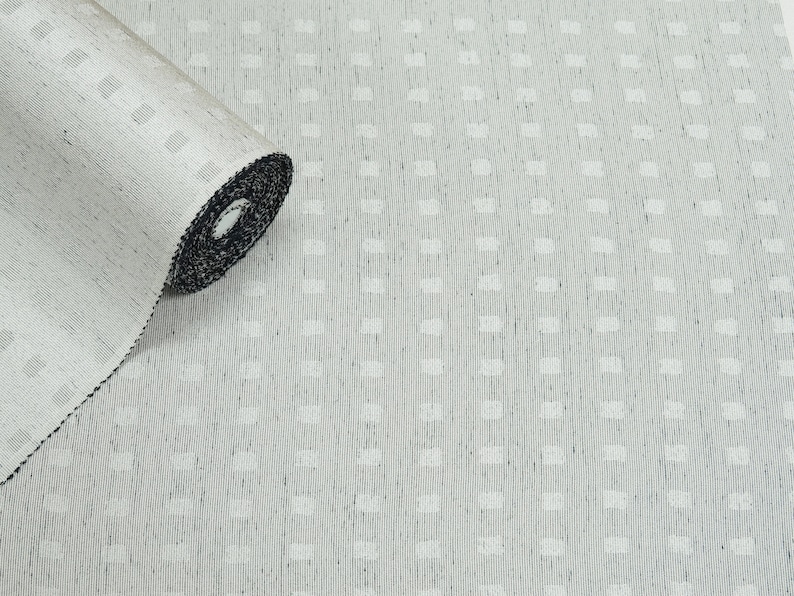May include: A roll of white fabric with a subtle textured pattern. The fabric has a black edge and is rolled up.
