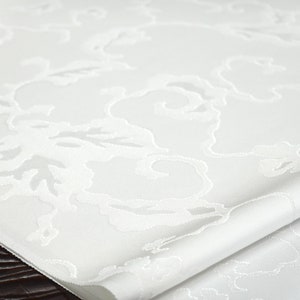 May include: White table runner with an embossed floral pattern. The runner is folded in half and has a smooth, silky texture.