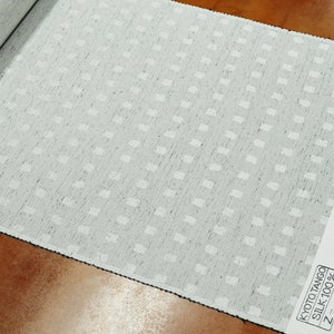 May include: A close-up of a white fabric with a subtle, repeating pattern of small squares. The fabric is labeled "Kyoto Tango Silk 100% Z-410".