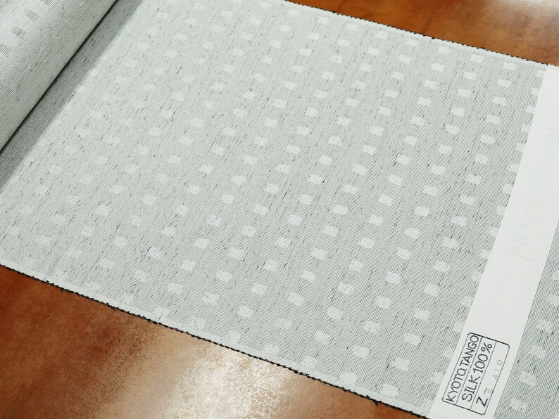 May include: A close-up of a white fabric with a subtle, repeating pattern of small squares. The fabric is labeled "Kyoto Tango Silk 100% Z-410".
