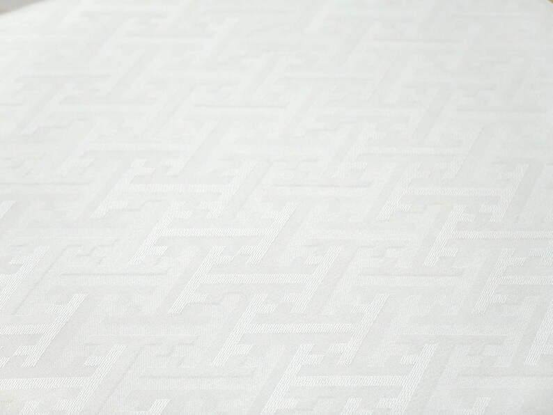 May include: White fabric with a subtle geometric pattern. The fabric has a smooth, slightly textured surface.
