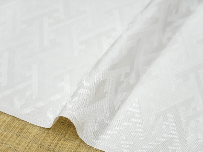 May include: White fabric with a subtle geometric pattern. The fabric is folded in half and has a smooth, silky texture.
