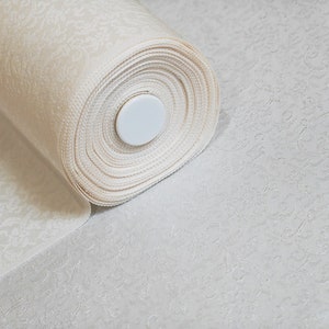 May include: A roll of white fabric with a delicate floral pattern. The fabric is rolled up and secured with a white plastic core.