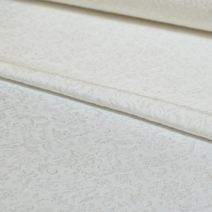 May include: White fabric with a subtle embossed floral pattern. The fabric is folded over, showing the texture of the pattern.