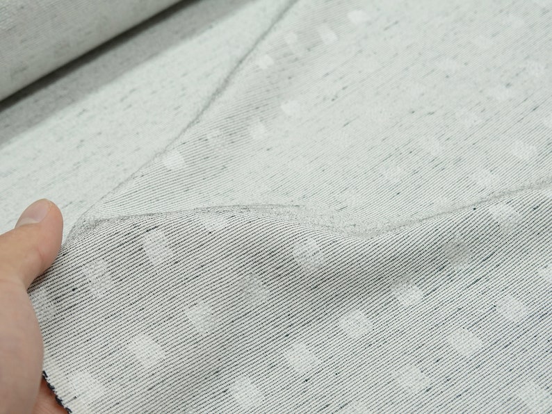 May include: Close-up of a white fabric with a subtle textured pattern. The fabric has a slightly grainy appearance and a subtle sheen.