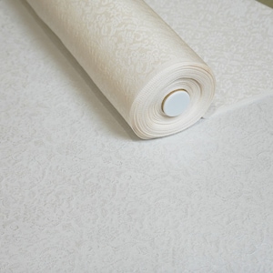 May include: A roll of white fabric with a delicate embossed pattern. The fabric is rolled up and secured with a white plastic cap.