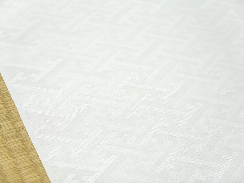 May include: White fabric with a subtle embossed pattern of repeating geometric shapes. The fabric has a smooth, slightly textured surface.