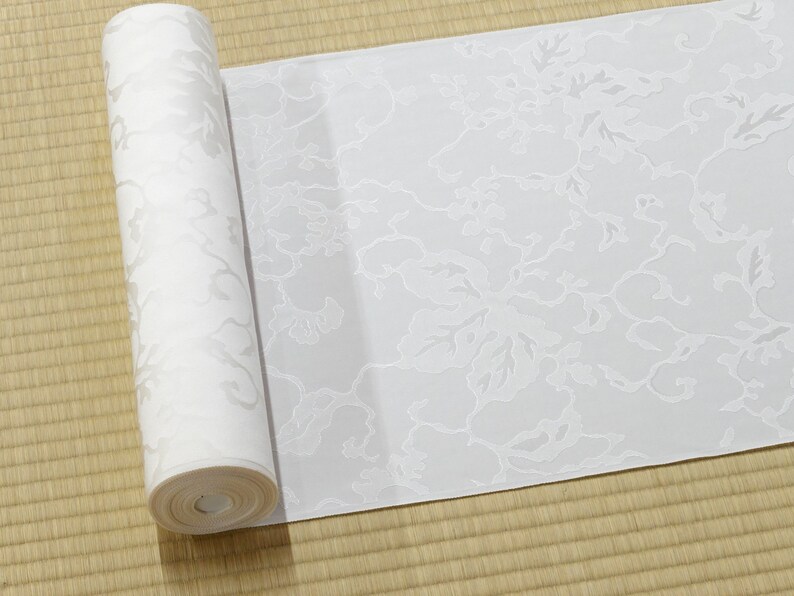 May include: A white roll of wallpaper with a floral pattern. The wallpaper has a subtle embossed texture.
