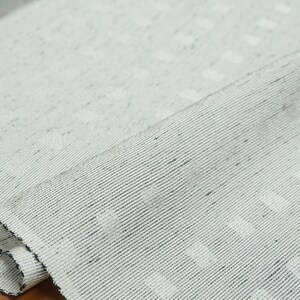 May include: Close-up of a white fabric with a subtle textured pattern. The fabric has a slightly rough, woven texture and a subtle sheen.