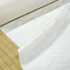 May include: White fabric with a geometric pattern, rolled up and displayed on a woven mat.