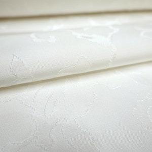 May include: White fabric with a subtle embossed floral pattern. The fabric is folded in half, showing the texture of the pattern.