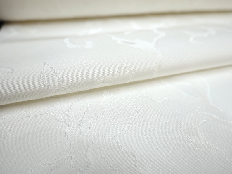 May include: White fabric with a subtle embossed floral pattern. The fabric is folded in half, showing the texture of the pattern.
