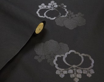 May include: Close-up of black fabric with a silver floral pattern. The fabric is rolled up and a wooden dowel is visible.