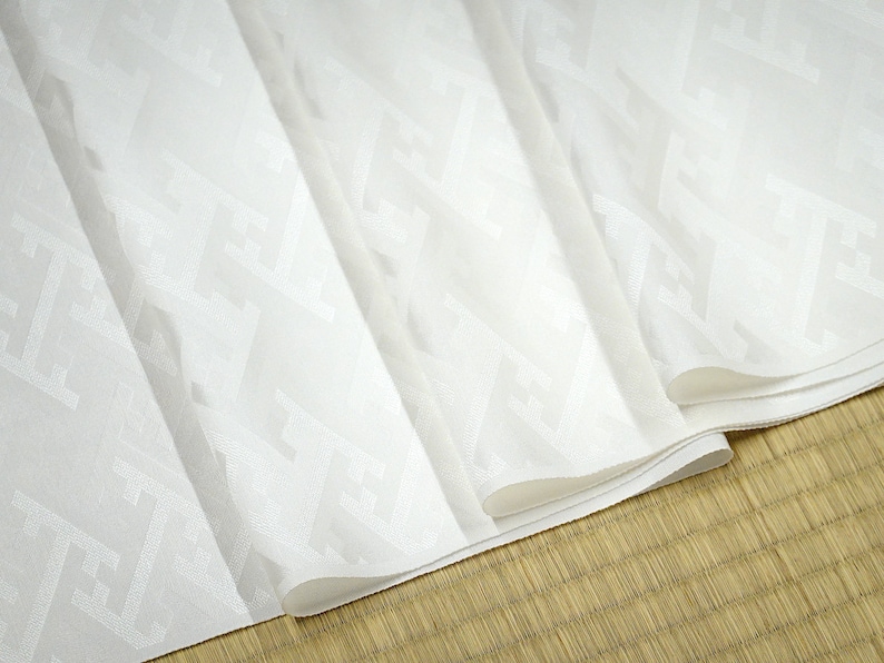May include: White fabric with a subtle embossed pattern. The fabric is folded several times, revealing the pattern.