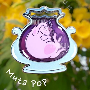 Puede incluir: Un tarro de vidrio morado con un borde plateado y una base azul claro. Dentro del tarro hay un gato rosa acurrucado durmiendo. El tarro tiene el texto "Muta POP" escrito debajo.
