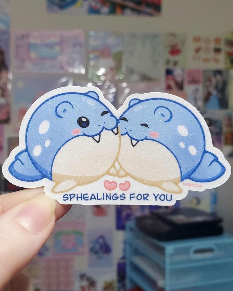 May include: A sticker featuring two cartoon seals, kissing. The seals are blue with white spots and have pink cheeks. The text "SPHEALINGS FOR YOU" is below the seals, with two pink hearts. The sticker has a white border.