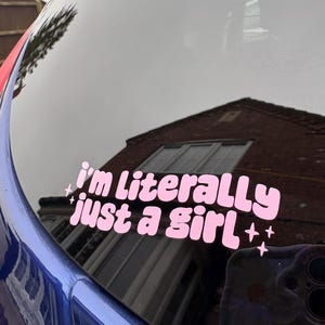 Peut inclure: Autocollant en vinyle rose avec le texte "I'm literally just a girl" dans une police r&eacute;tro, avec des &eacute;toiles. L'autocollant est appliqu&eacute; sur une vitre de voiture, refl&eacute;tant l'environnement. La voiture est bleue.