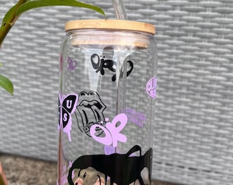 Peut inclure: Un gobelet en verre transparent avec un couvercle en bambou et une paille en verre. Le gobelet est décoré de graphiques noirs et violets, dont un papillon, des lèvres et les lettres "OR" et "US".