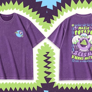 Könnte beinhalten: Ein violettes T-Shirt mit kurzen Ärmeln und einer kleinen blauen Augengrafik auf der linken Brust. Die Rückseite zeigt eine große Grafik einer Kartoffel mit Händen über einer Kristallkugel und den Text MAGIC POTATO SEES ALL KNOWS NUTHIN'.