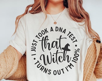 May include: Cream-colored t-shirt with a black circular graphic that reads "I just took a DNA test, turns out I'm 100% that Witch." A witch hat graphic is in the center. The shirt is part of a Halloween or witch-themed collection.