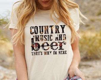 May include: A woman wearing a beige t-shirt with the text "Country Music and Beer That's Why I'm Here" in black lettering with a floral pattern. She is wearing a brown hat and a red and black plaid shirt tied around her waist.