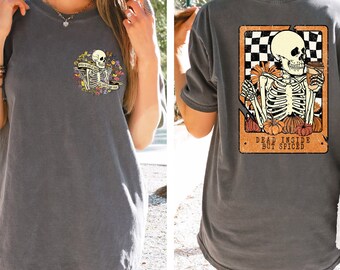 Può includere: T-shirt grigio scuro con grafica a scheletro sul davanti e sul retro. La grafica anteriore mostra uno scheletro con fiori e la scritta "But first, coffee". La grafica posteriore presenta uno scheletro con una tazza di caffè e la scritta "Dead Inside But Spiced".