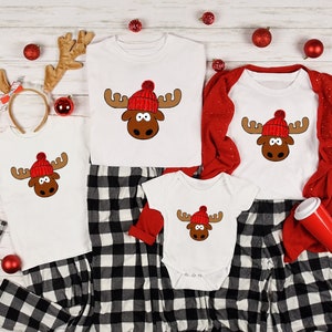 May include: A family of four matching pajamas with a red and white plaid pattern. Each pajama top features a white moose with a red Santa hat. The pajamas are perfect for a festive Christmas celebration.