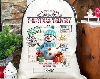 Puede incluir: Un saco de Navidad de lona blanca con un cordón de ajuste negro. El saco tiene un diseño festivo con un muñeco de nieve, notas musicales y el texto "A Very Merry Christmas Delivery".