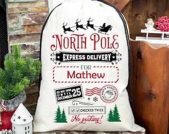 Puede incluir: Un saco de Santa de lona blanca con cordón de ajuste negro, con el texto "NORTH POLE EXPRESS DELIVERY" y un nombre personalizado "Mathew". El saco tiene un sello rojo y negro "NO ABRIR HASTA EL 25 DE DICIEMBRE", una cinta roja y blanca a rayas y un gráfico de árbol verde.