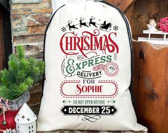 Puede incluir: Un saco de Santa de lona blanca con ribete negro y texto rojo y verde. El texto dice "Christmas Express Delivery for Sophie Do Not Open Before December 25". Hay una ilustración en blanco y negro del trineo de Santa con renos volando por el aire.