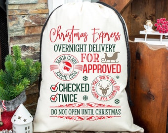 Puede incluir: Bolsa de regalo de Navidad blanca con cordón de ajuste negro. La bolsa tiene texto rojo y verde que dice "Christmas Express Overnight Delivery For Approved" con un sello de Santa Claus y un sello de reno.