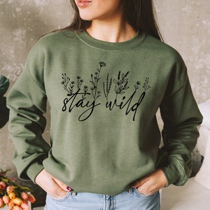 May include: A green sweatshirt with the text "stay wild" in black script with a line drawing of flowers and leaves.