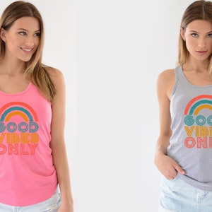 May include: Two women wearing tank tops with a rainbow and the text "Good Vibes Only" printed on the front. The tank top on the left is pink and the tank top on the right is gray.